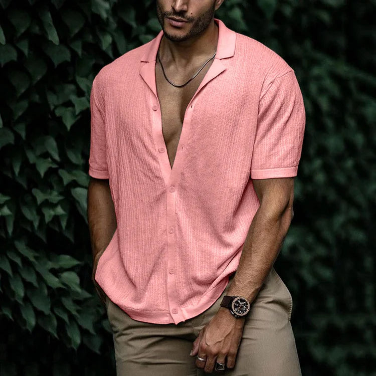 Man wearing pink short sleeve button-down shirt with open collar, paired with khaki pants and a watch.