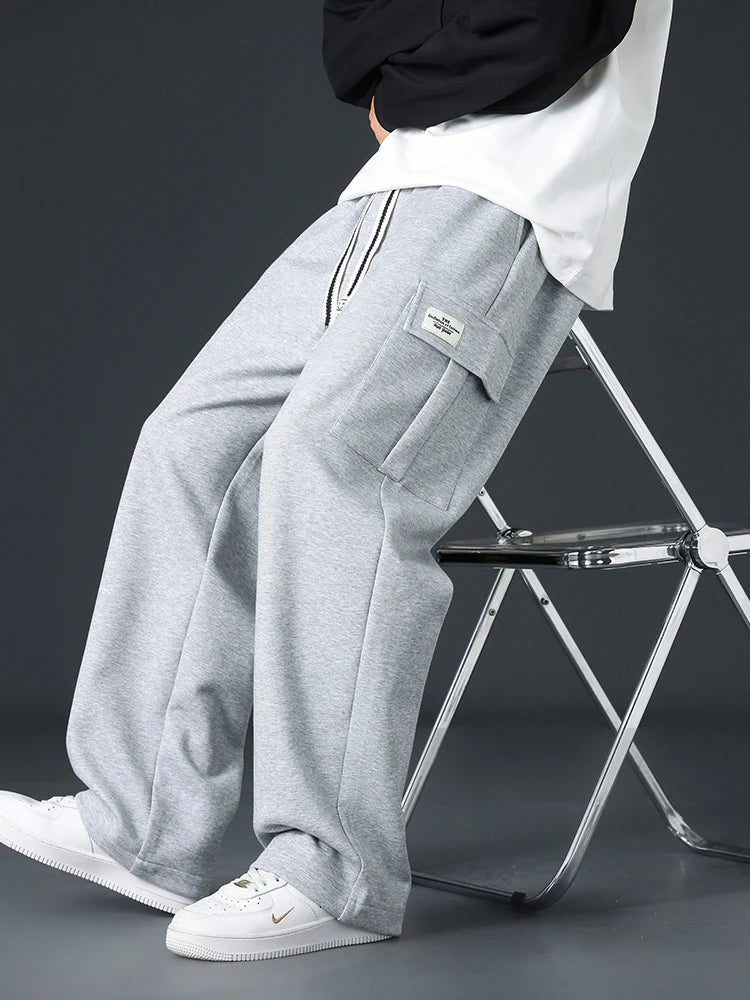 Men's gray wide-leg cargo sweatpants with side pockets and drawstring waist, worn with white sneakers