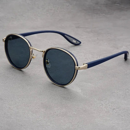 Round blue and gold UV400 sunglasses with dark lenses, metal frame, and navy blue temples on gray surface.