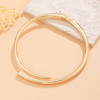 Gold tone open cuff bangle bracelet with modern minimalist design displayed on beige background with flowers