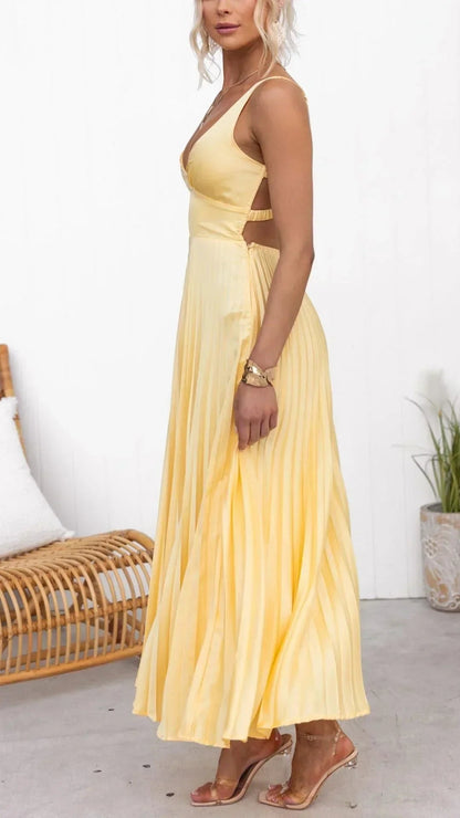 Yellow pleated maxi dress with deep V-neck, side cutouts, and spaghetti straps, paired with clear heeled sandals.