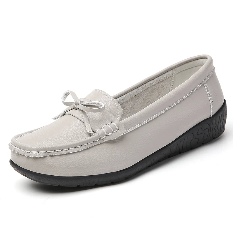 Light gray women's leather slip-on loafers with decorative bow detail and black rubber sole on white background