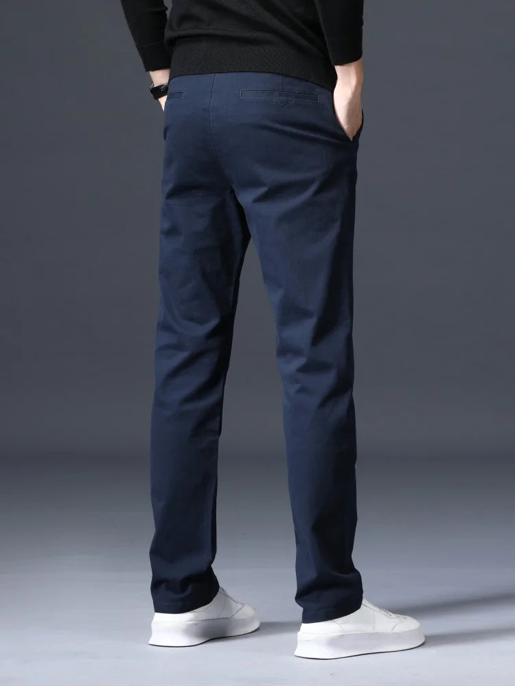 Man wearing slim-fit navy blue cotton dress pants with white sneakers and black sweater, rear view.
