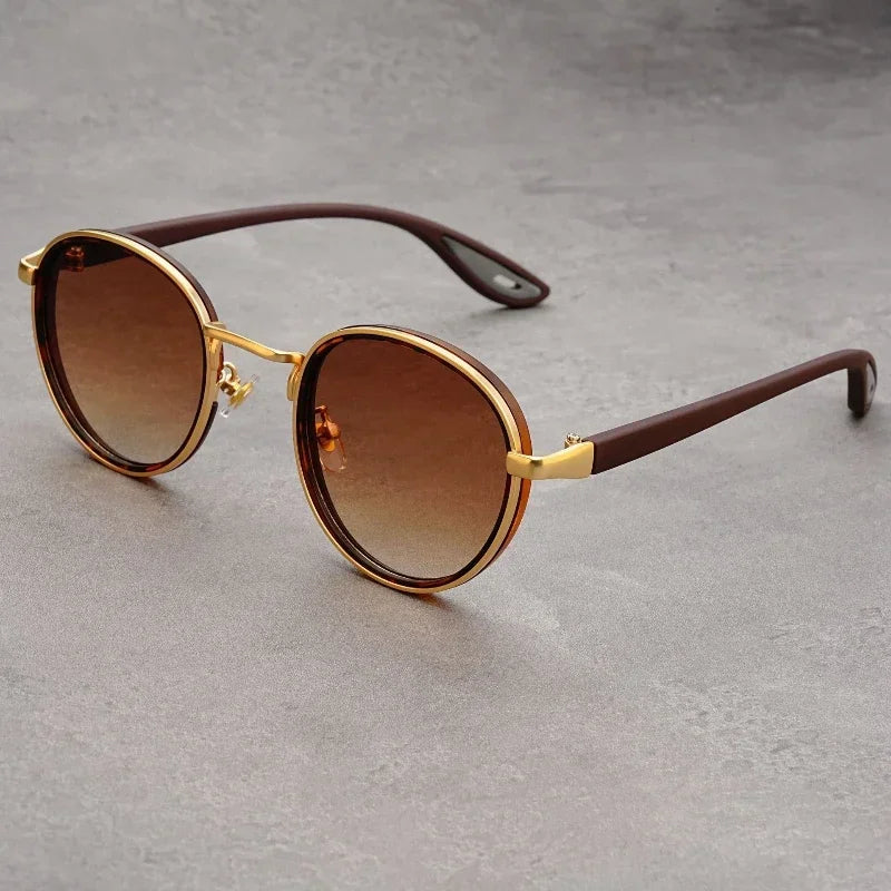 Round brown gradient UV400 sunglasses with gold metal accents and brown arms on gray surface