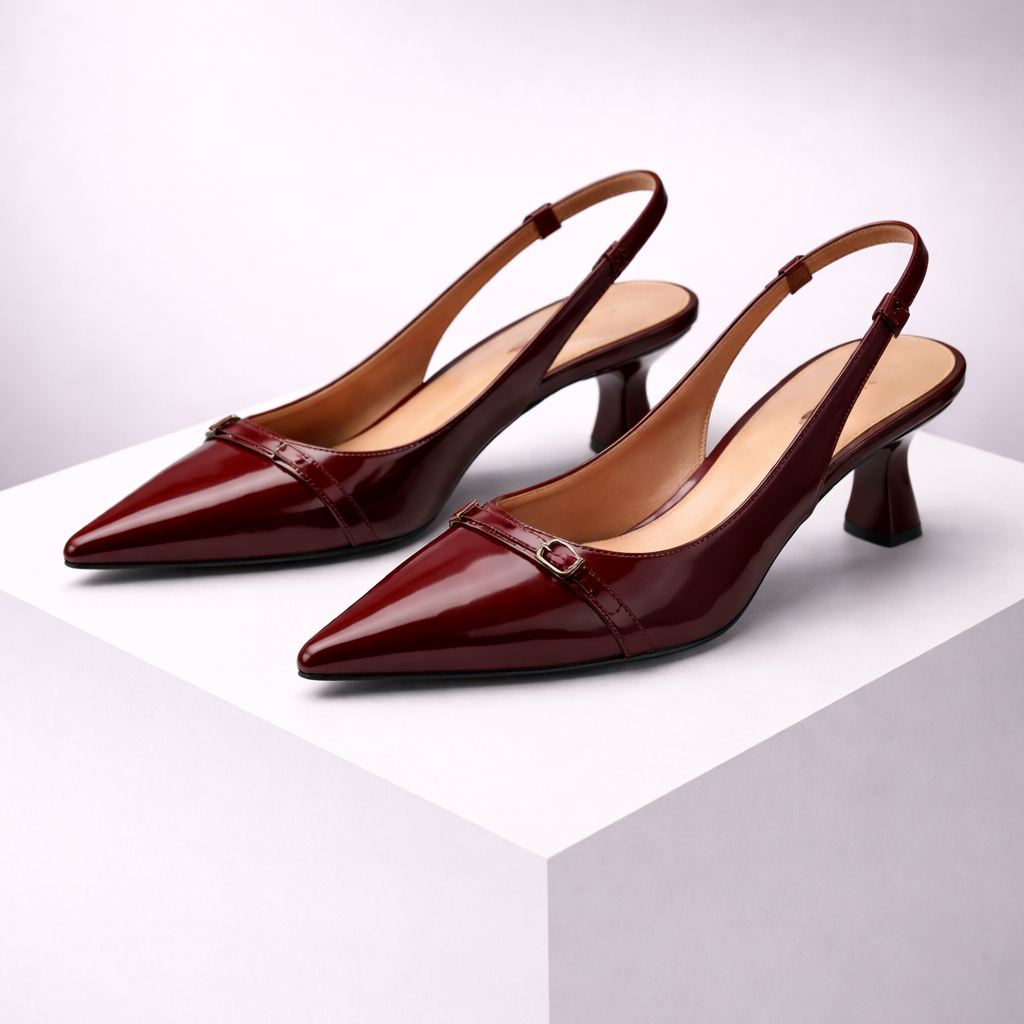 Burgundy patent leather pointed-toe slingback heels with gold buckle detail and kitten heel, displayed on white platform