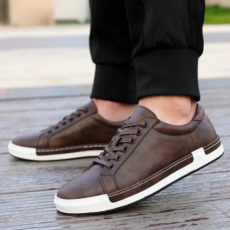 Men's brown leather lace-up sneakers with white sole and low-top design on wooden deck