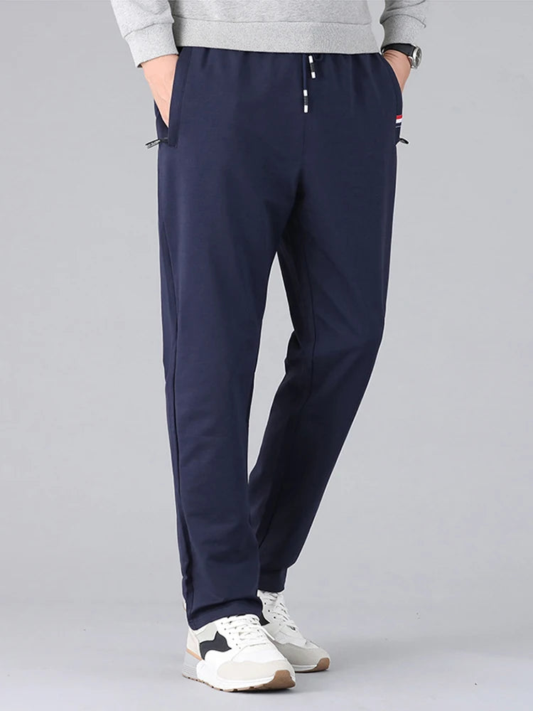 Navy blue men's cotton drawstring sweatpants with zip pockets, worn with gray sweatshirt and white sneakers
