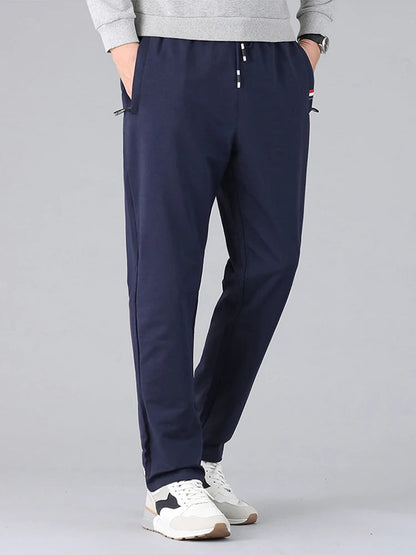 Navy blue men's cotton drawstring sweatpants with zip pockets, worn with gray sweatshirt and white sneakers