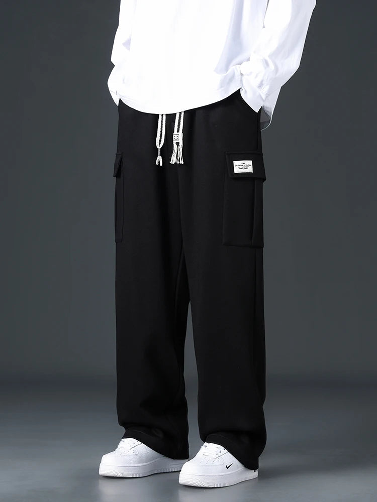 Black wide-leg men's cargo sweatpants with drawstring waist, side pockets, and label patch, paired with white sneakers.