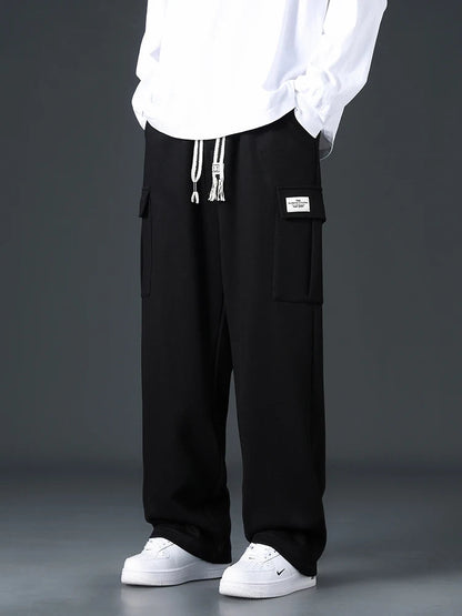 Black wide-leg men's cargo sweatpants with drawstring waist, side pockets, and label patch, paired with white sneakers.