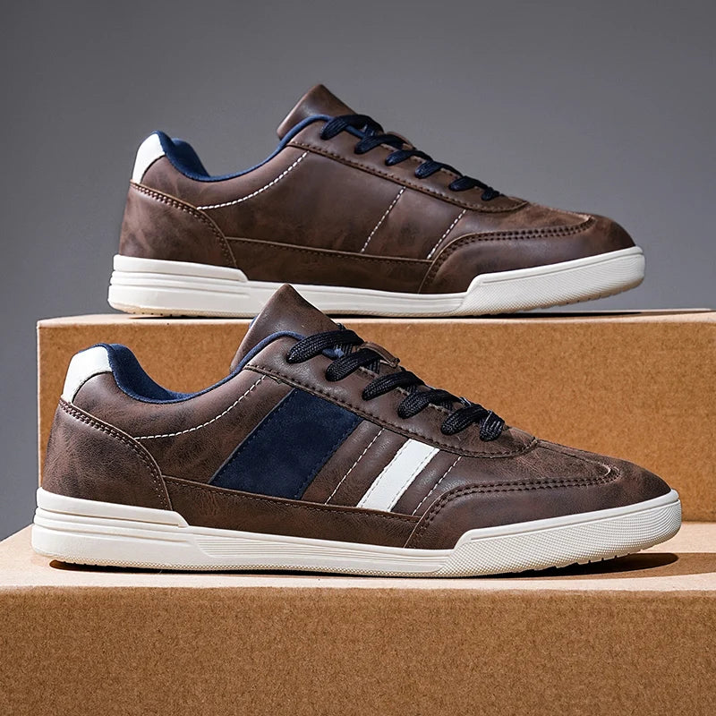 Brown leather low-top men's sneakers with navy blue accents, white sole, and dark laces displayed on cardboard box