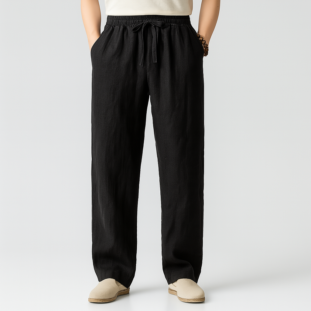 Black men's linen drawstring pants with elastic waistband, relaxed fit, side pockets, worn with beige slip-on shoes.
