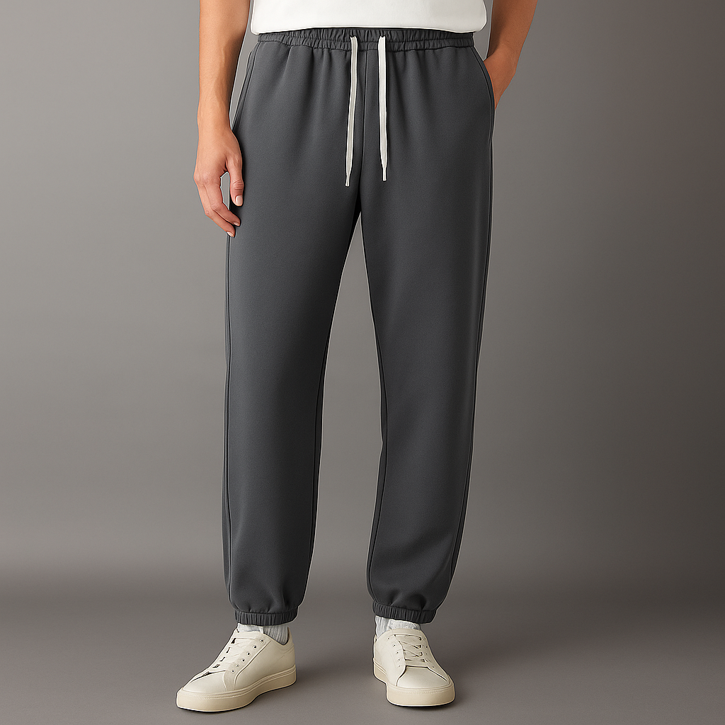Men's dark gray Tove Cotton Drawstring Joggers with white drawstring, elastic waistband and cuffs, worn with white sneakers.