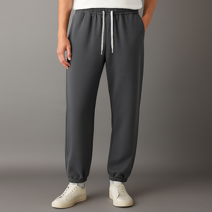 Men's dark gray Tove Cotton Drawstring Joggers with white drawstring, elastic waistband and cuffs, worn with white sneakers.