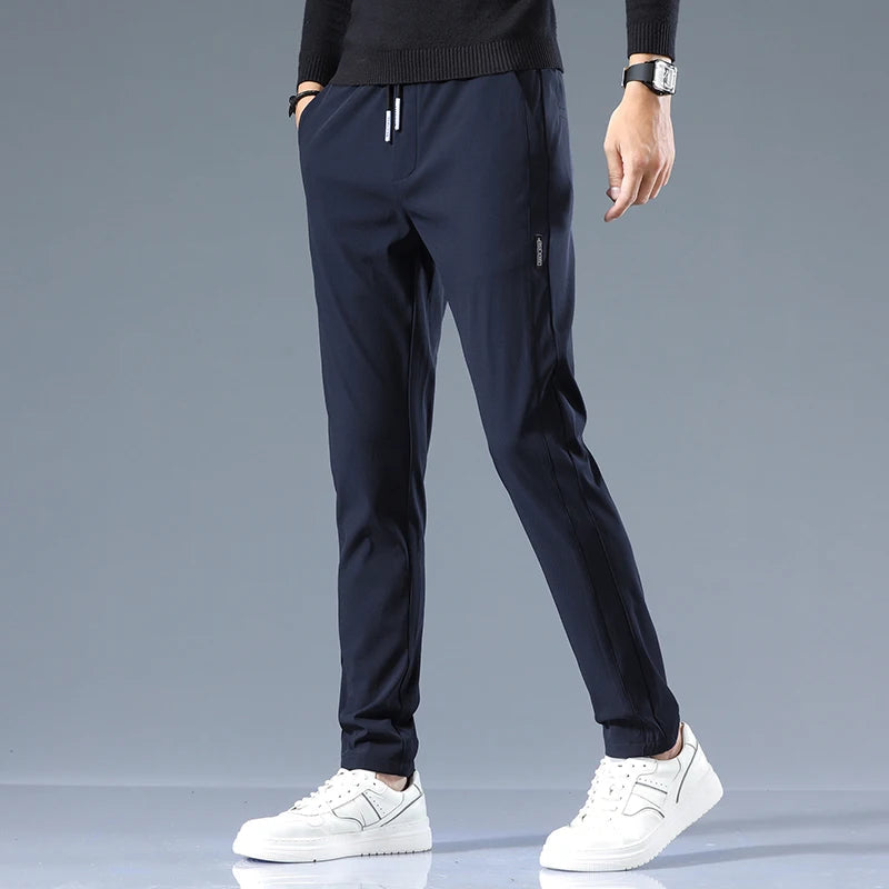 Navy blue men's cotton drawstring joggers with side pockets, worn with white sneakers and black sweater, slim fit style.