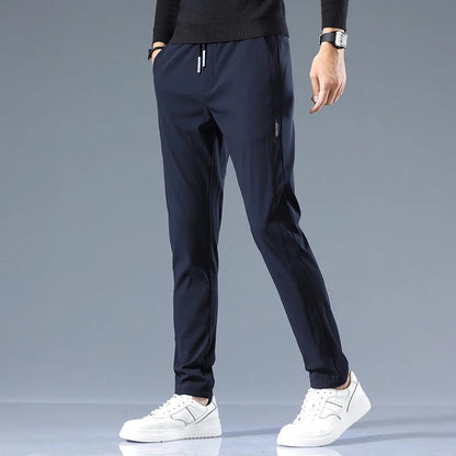 Navy blue men's cotton drawstring joggers with side pockets, worn with white sneakers and black sweater, slim fit style.
