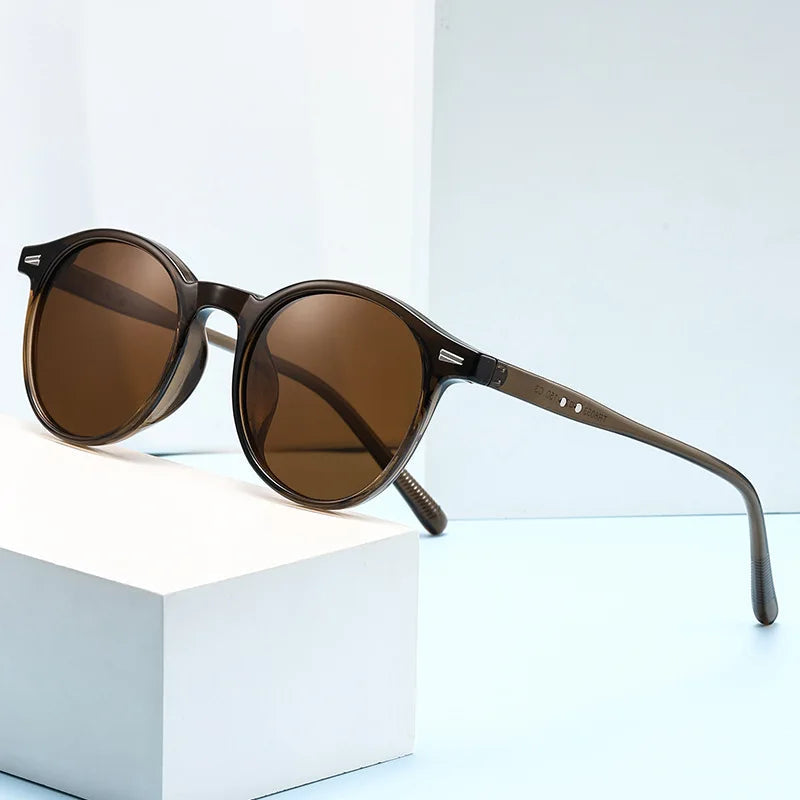 Brown round acetate sunglasses with tortoiseshell temples displayed on white block against light blue background