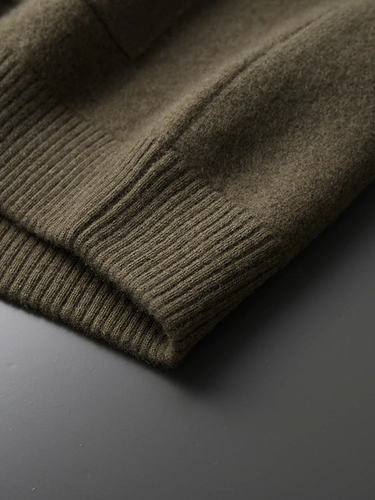 Close-up of olive green merino wool cardigan jacket cuff showing ribbed knit trim detail on gray surface