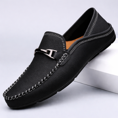 Black leather men's slip-on loafer with white contrast stitching, metal horsebit buckle, and tan interior lining.