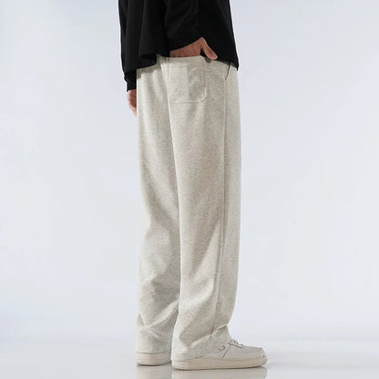Man wearing light gray cotton wide-leg relaxed-fit sweatpants with white sneakers and black long-sleeve top, side view.