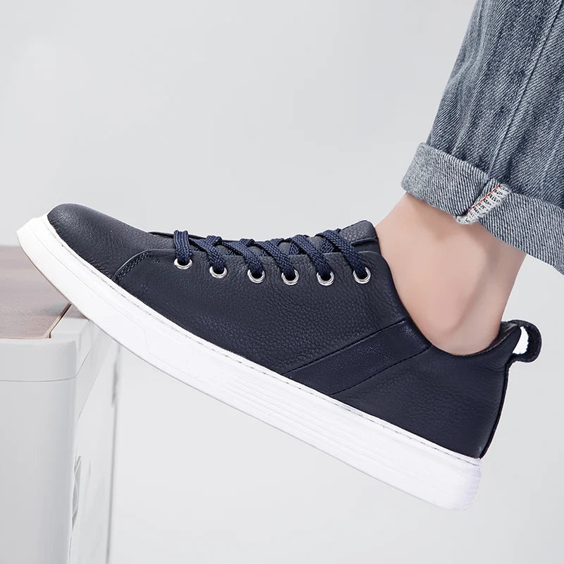 Navy blue leather lace-up low-top men's sneakers with white sole, worn with rolled cuff jeans, side profile view.