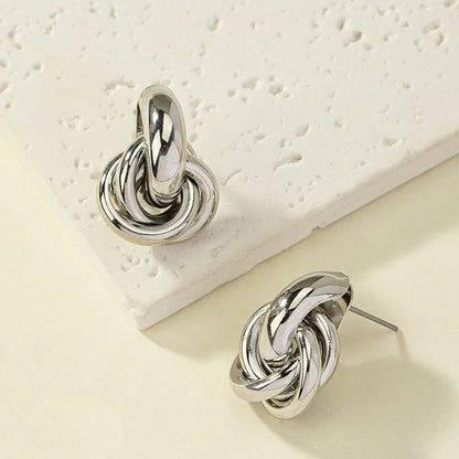 Silver interlocked knot stud earrings with twisted multi-ring design, shown on white textured surface