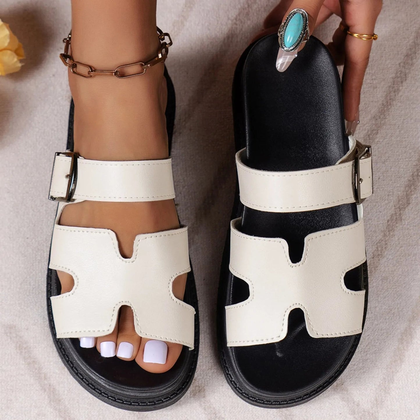 Women's cream vegan leather slide sandals with H-cutout straps, silver buckles, and black platform sole.