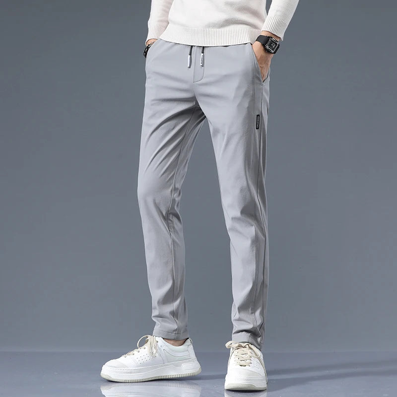 Men's light gray cotton drawstring joggers with slim fit, worn with white sneakers and cream sweater.