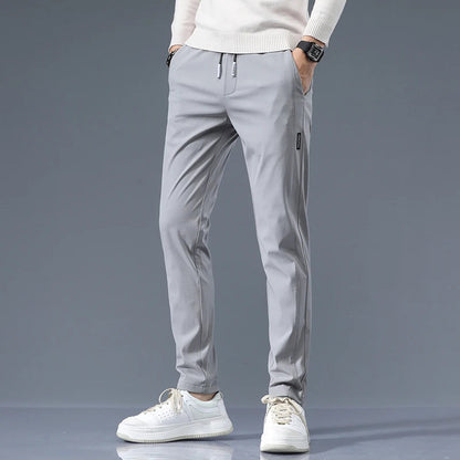 Men's light gray cotton drawstring joggers with slim fit, worn with white sneakers and cream sweater.