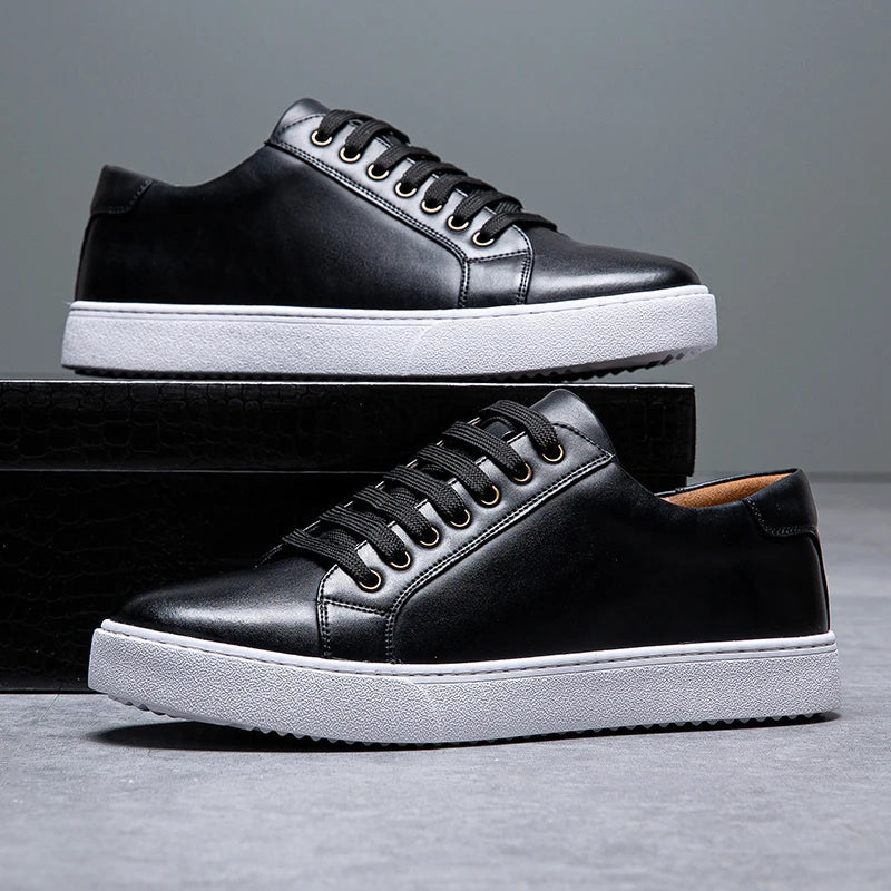 Black leather lace-up men's sneakers with white platform sole and gold eyelets, displayed in pairs on dark box