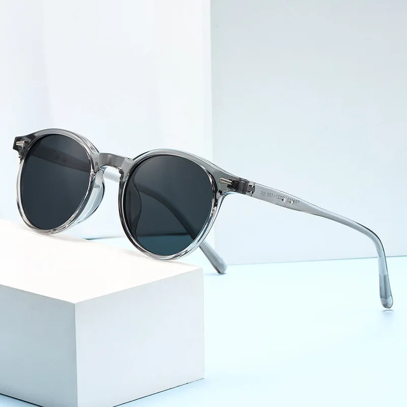 Round acetate sunglasses with transparent gray frames, dark lenses, and textured temples displayed on white surface