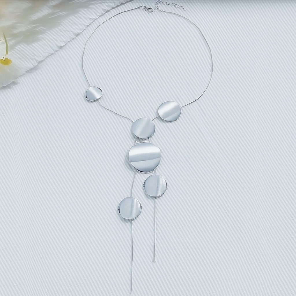 Silver asymmetric disc chain necklace with multiple graduated circular pendants and tassel ends on white background