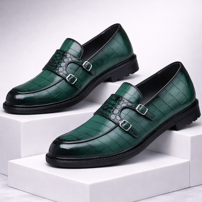 Green croc-embossed leather double monk strap loafers with silver buckles and black rubber soles displayed on white blocks