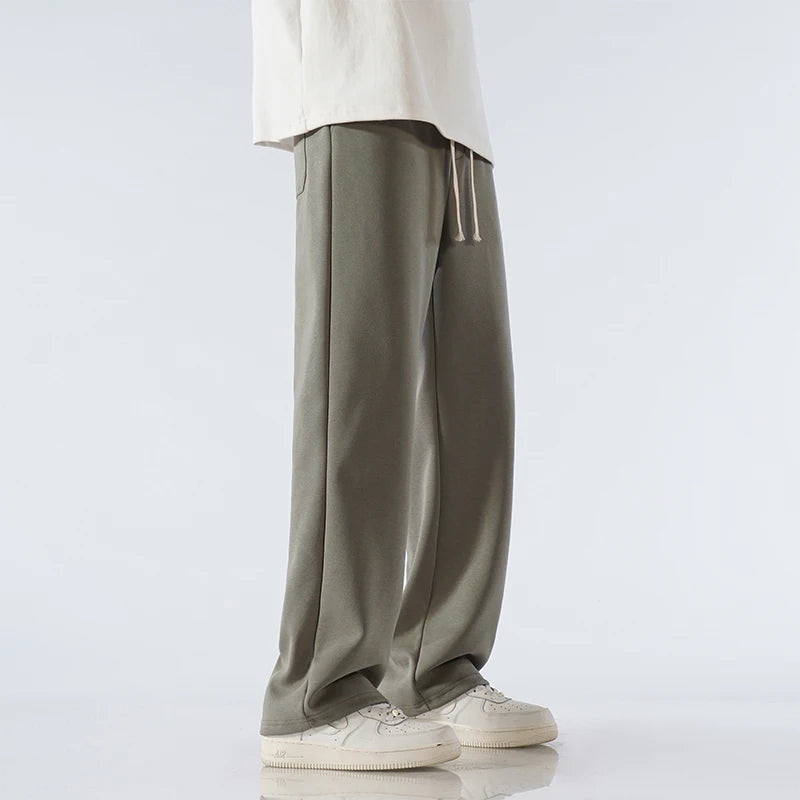 Man wearing sage green wide-leg relaxed-fit cotton drawstring pants with white sneakers and cream top, side view.