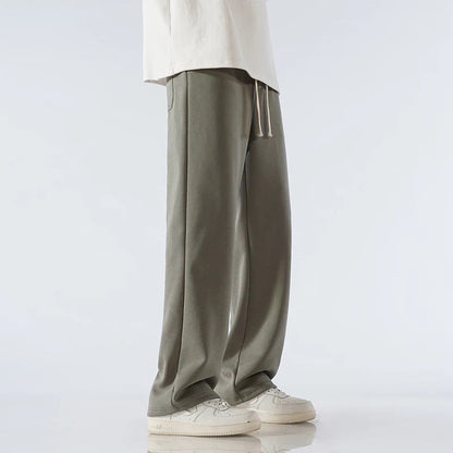 Man wearing sage green wide-leg relaxed-fit cotton drawstring pants with white sneakers and cream top, side view.