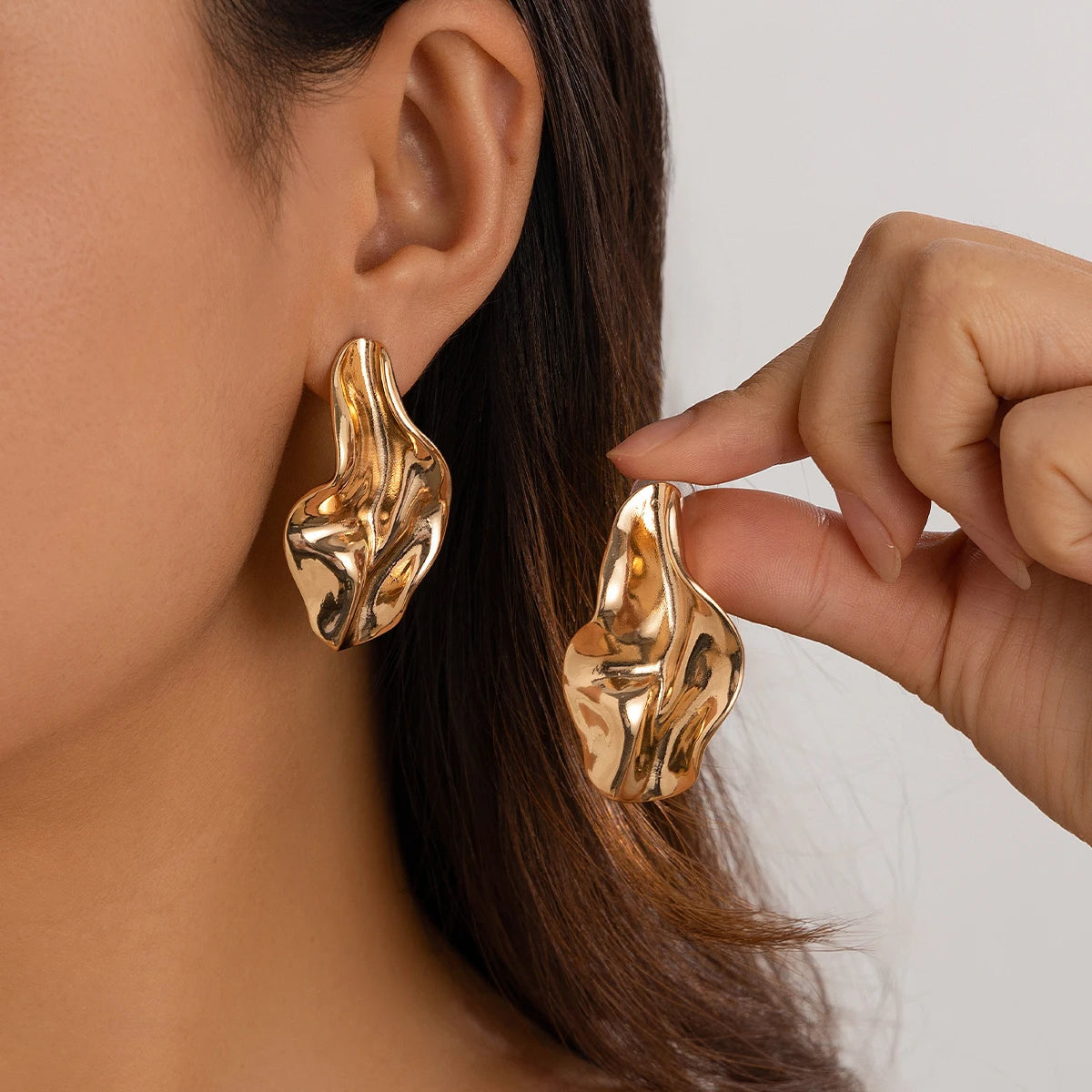 Chunky gold twisted abstract drop earrings on woman's ear, modern statement jewelry for women