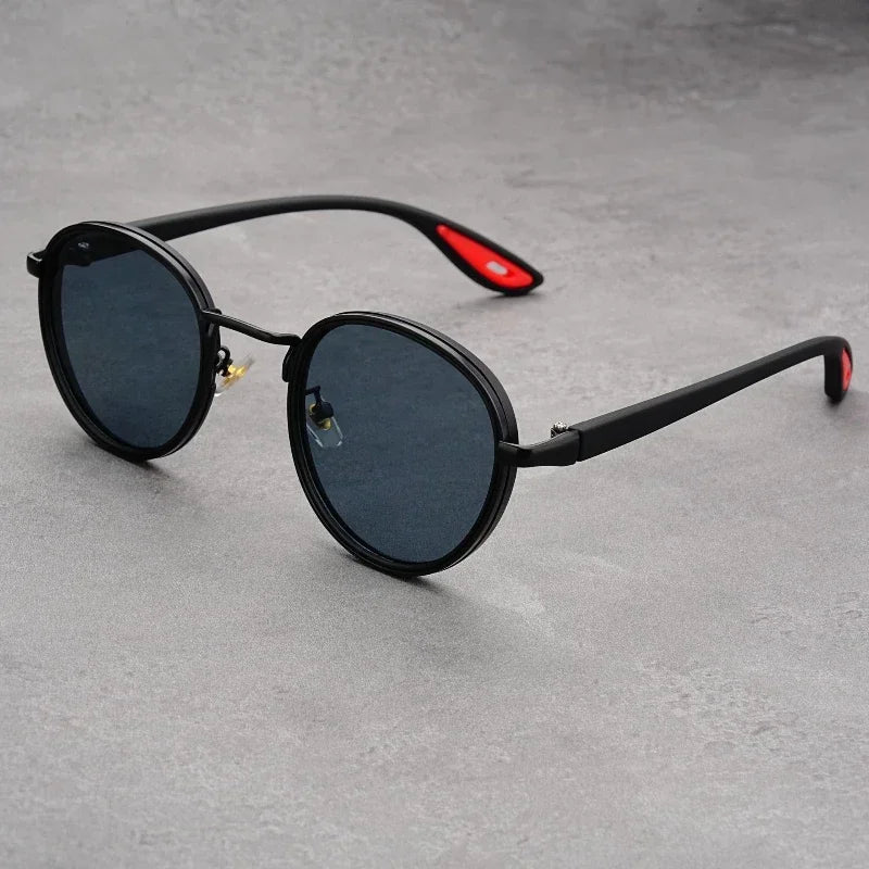 Black round frame UV400 sunglasses with red temple accents and dark polarized lenses on gray surface