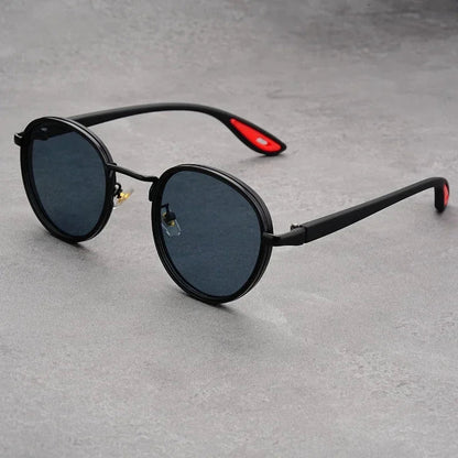Black round frame UV400 sunglasses with red temple accents and dark polarized lenses on gray surface