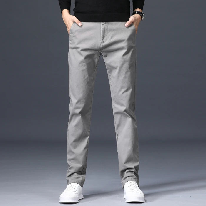 Men's slim-fit light gray cotton dress pants worn with white sneakers and black sweater, front view on model.