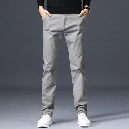 Men's slim-fit light gray cotton dress pants worn with white sneakers and black sweater, front view on model.