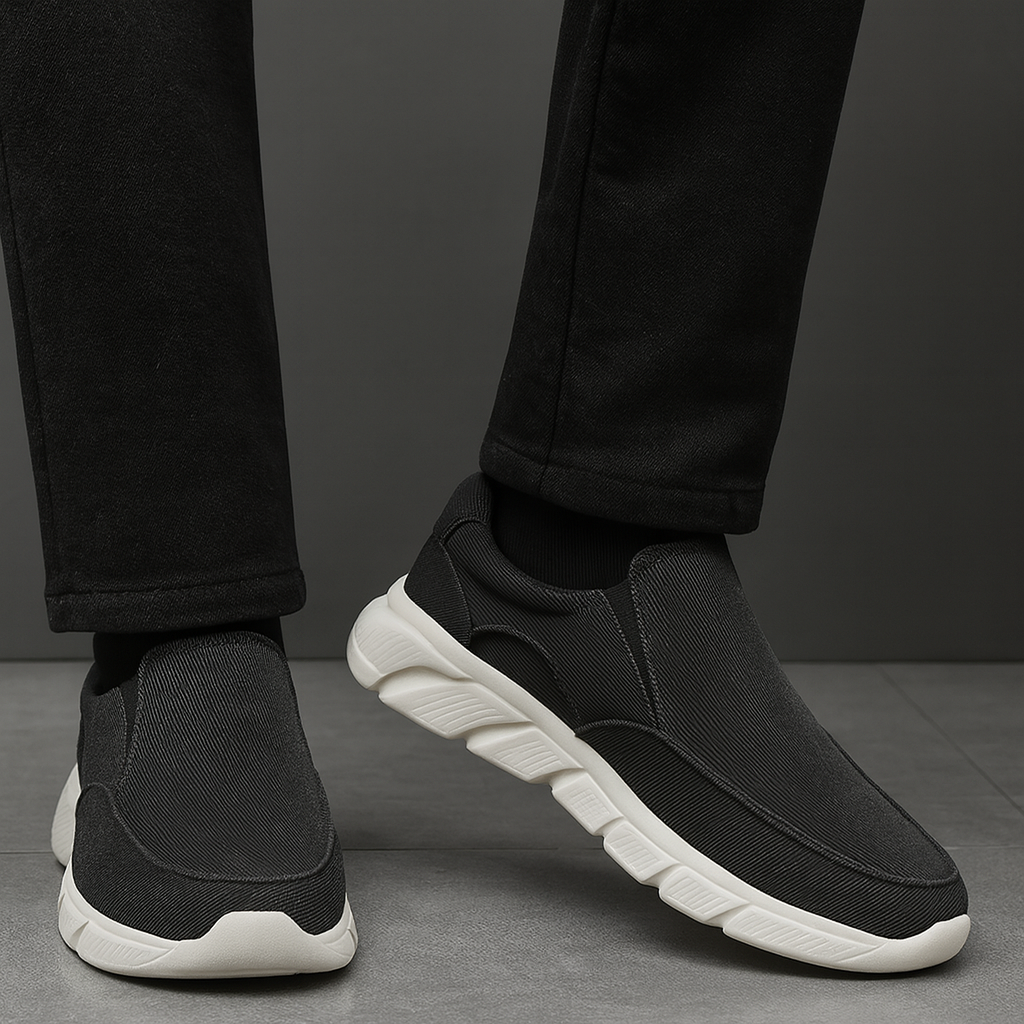 Men's black corduroy slip-on sneakers with white chunky sole, paired with black pants, shown from ankle down.