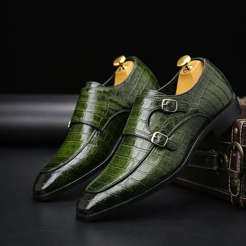 Green crocodile-embossed leather men's double monk strap dress shoes with gold shoe trees on dark background