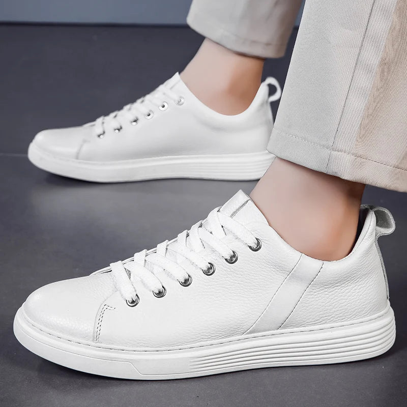 White leather lace-up low-top men's sneakers with silver eyelets and white rubber sole, worn with beige pants