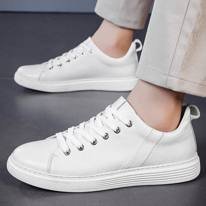 White leather lace-up low-top men's sneakers with silver eyelets and white rubber sole, worn with beige pants