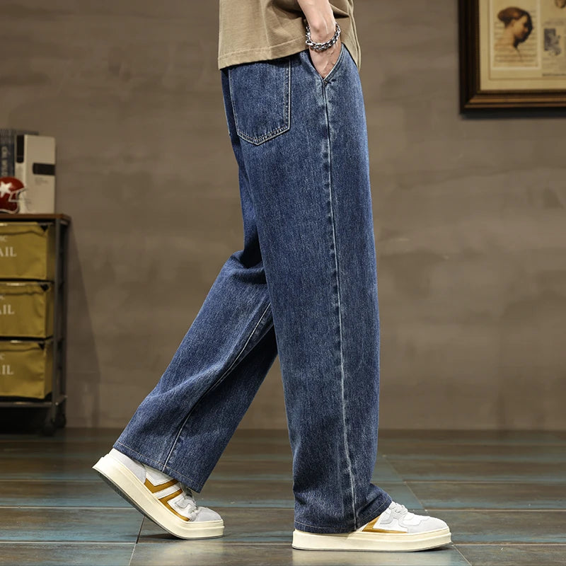 Men's wide-leg blue denim jeans with drawstring waist, paired with white sneakers and a tan t-shirt, side view.
