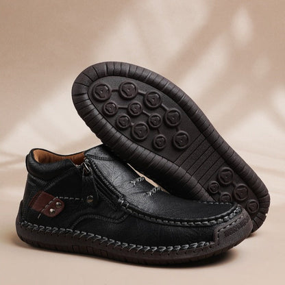 Black leather men's slip-on ankle boots with side zipper, hand-stitching detail, and rubber grip sole displayed on beige background