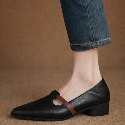 Black leather pointed-toe women's flats with brown T-strap accent and low block heel, styled with cropped blue jeans.