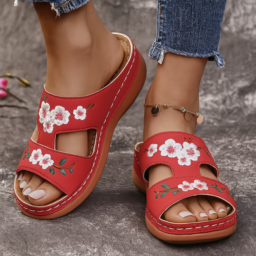 Red slip-on platform sandals with white floral embroidery, open toe, worn with distressed jeans and gold anklet bracelet.