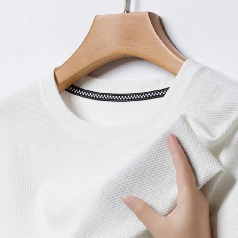 White men's waffle knit crewneck t-shirt on wooden hanger, hand demonstrating soft fabric texture.