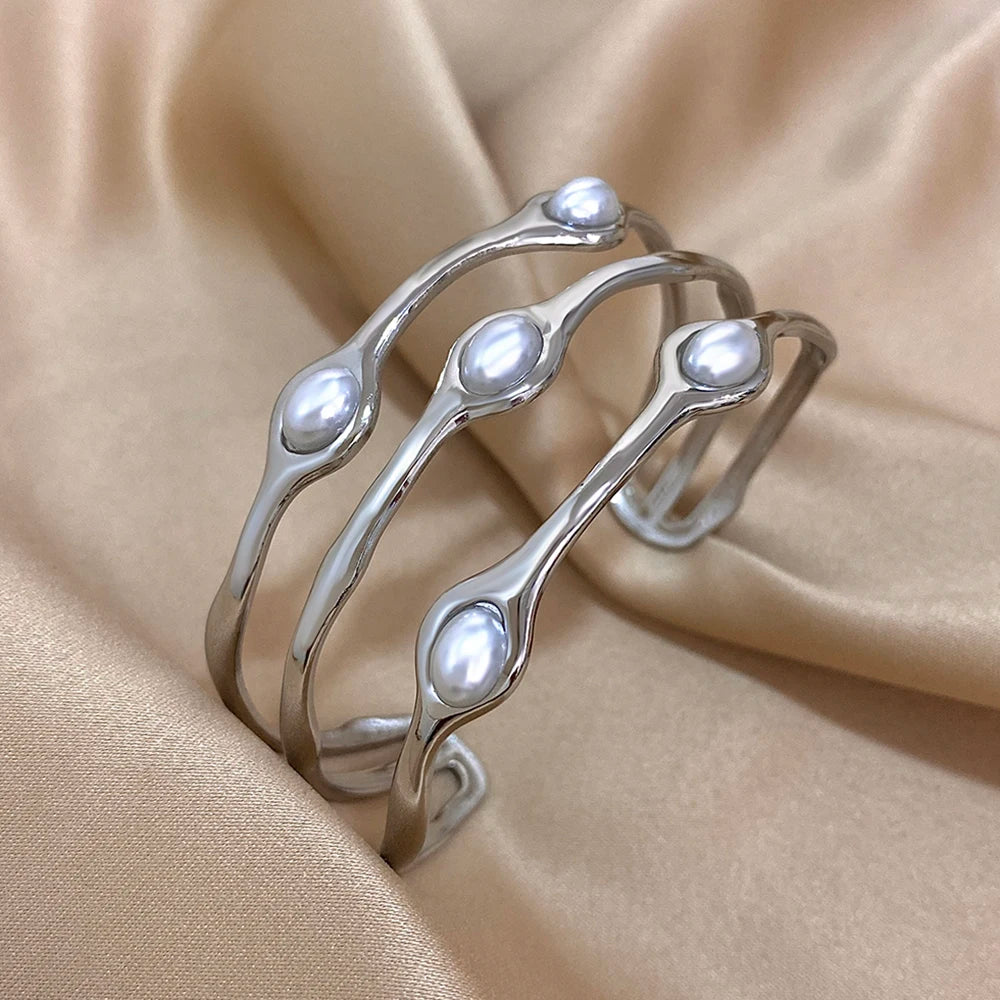 Silver tone open cuff bangle bracelet with three wavy rows and embedded oval white pearls on satin fabric